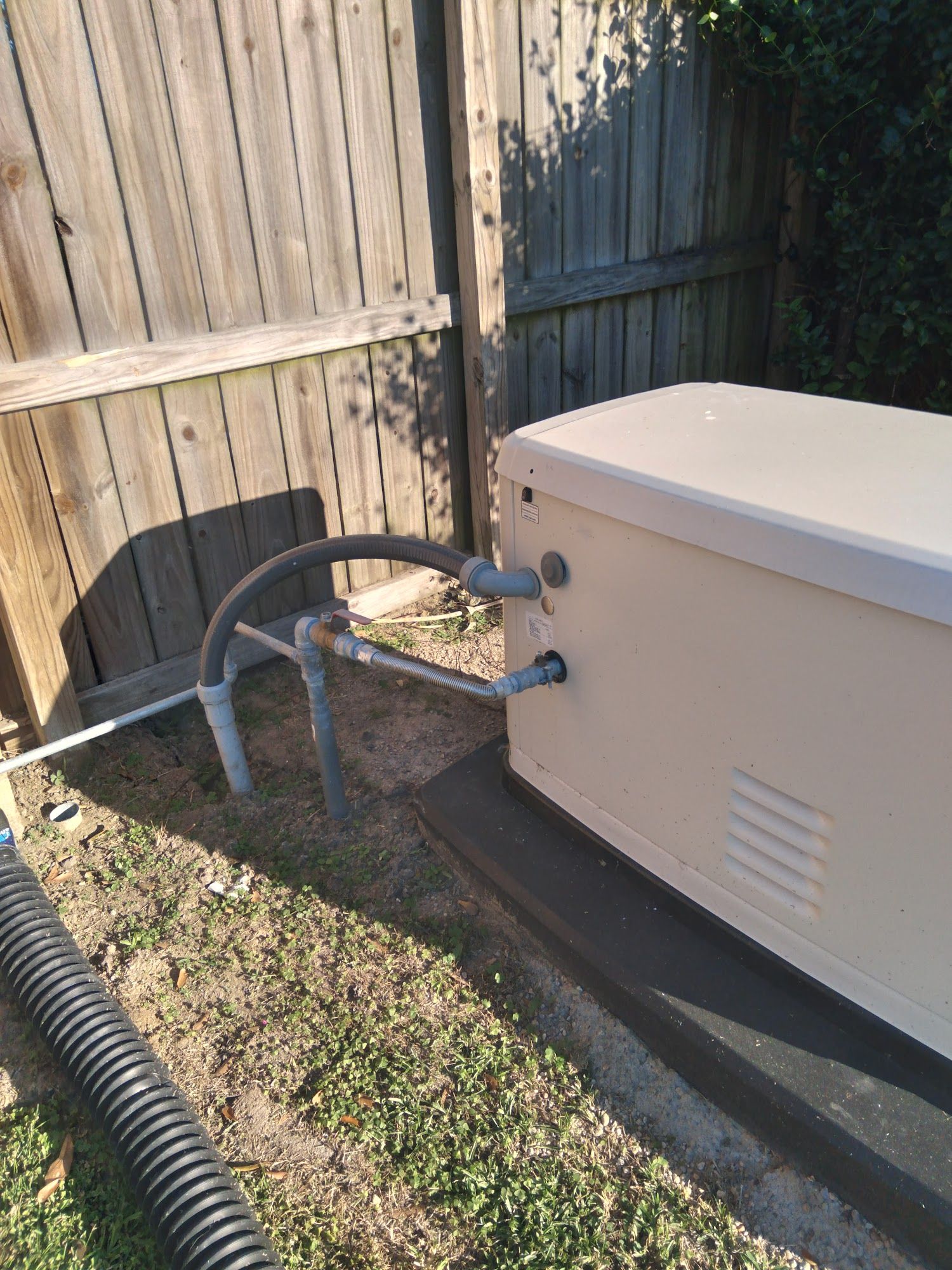A generator is sitting in the grass next to a wooden fence.