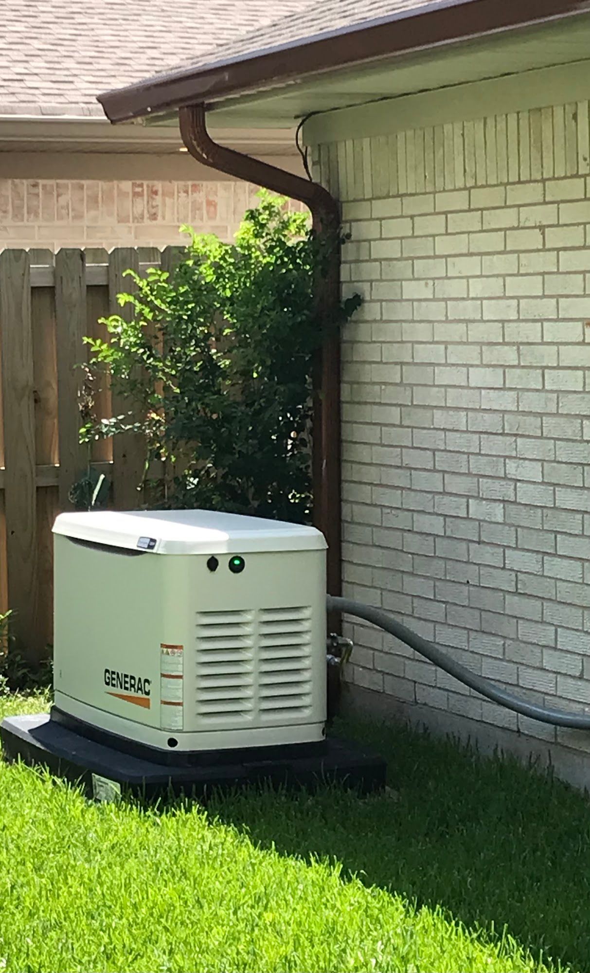 A generator is sitting on the side of a brick house.
