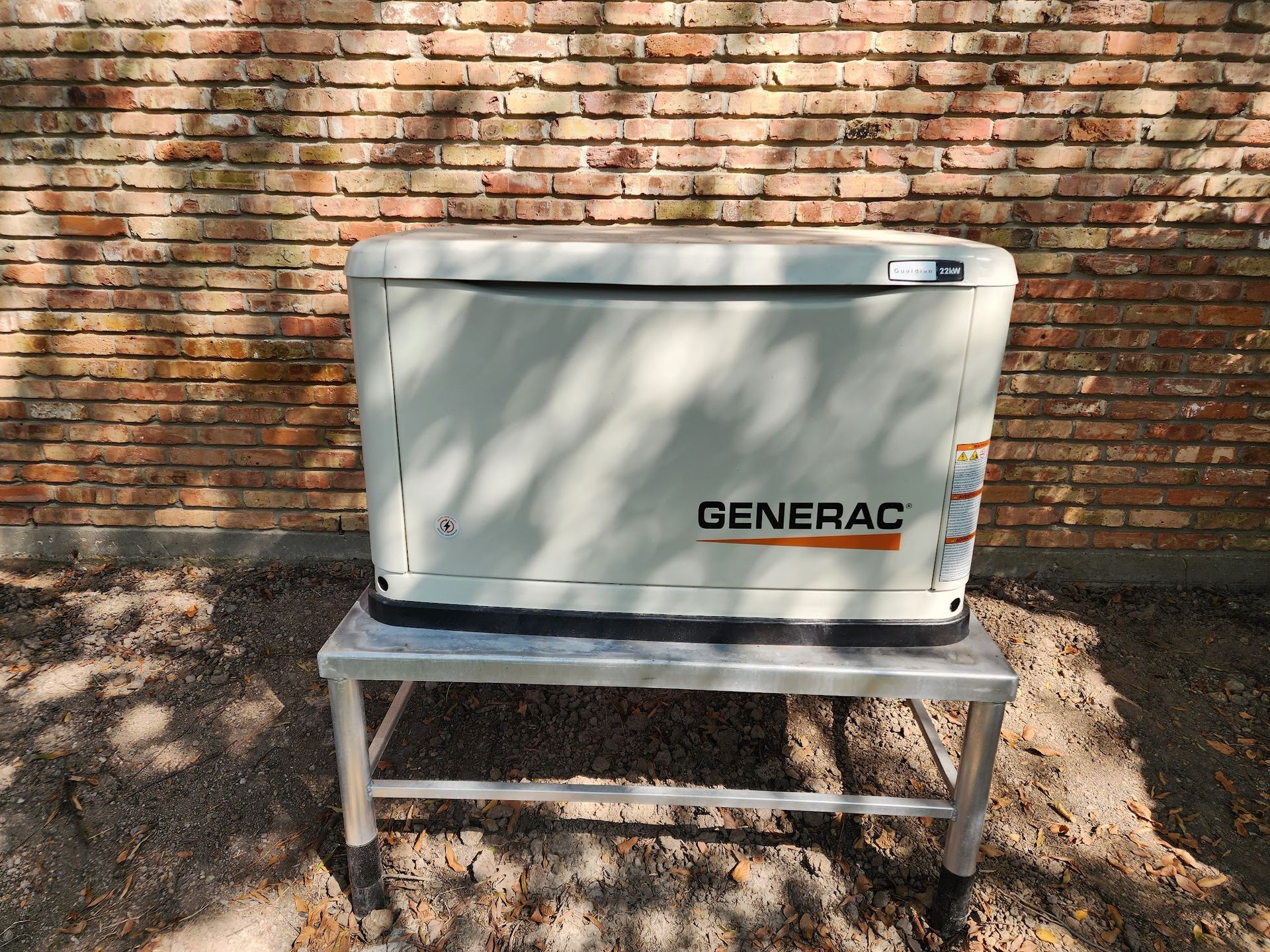 A generator is sitting on a metal stand in front of a brick wall.