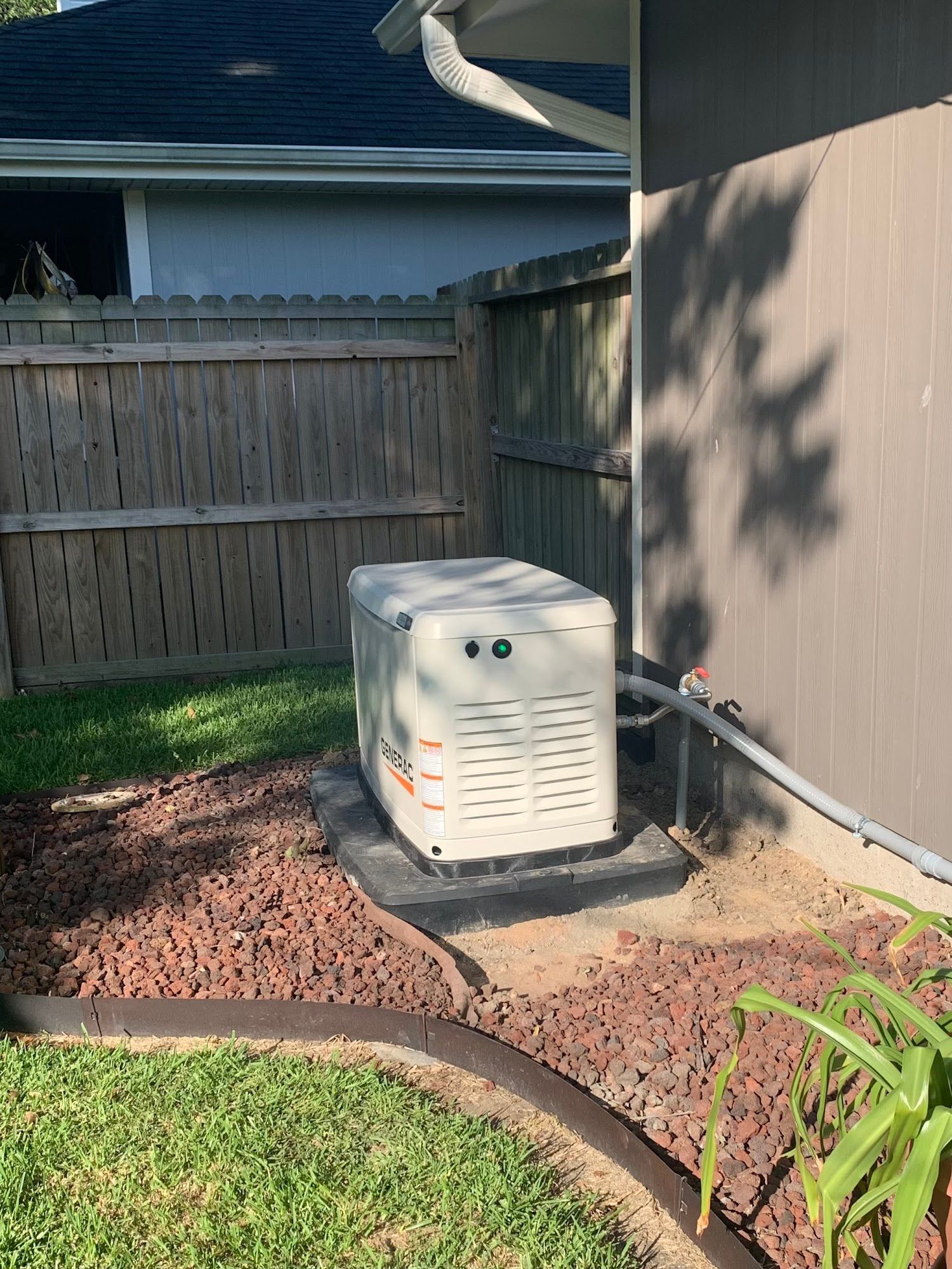 A generator is sitting on the side of a house next to a fence.