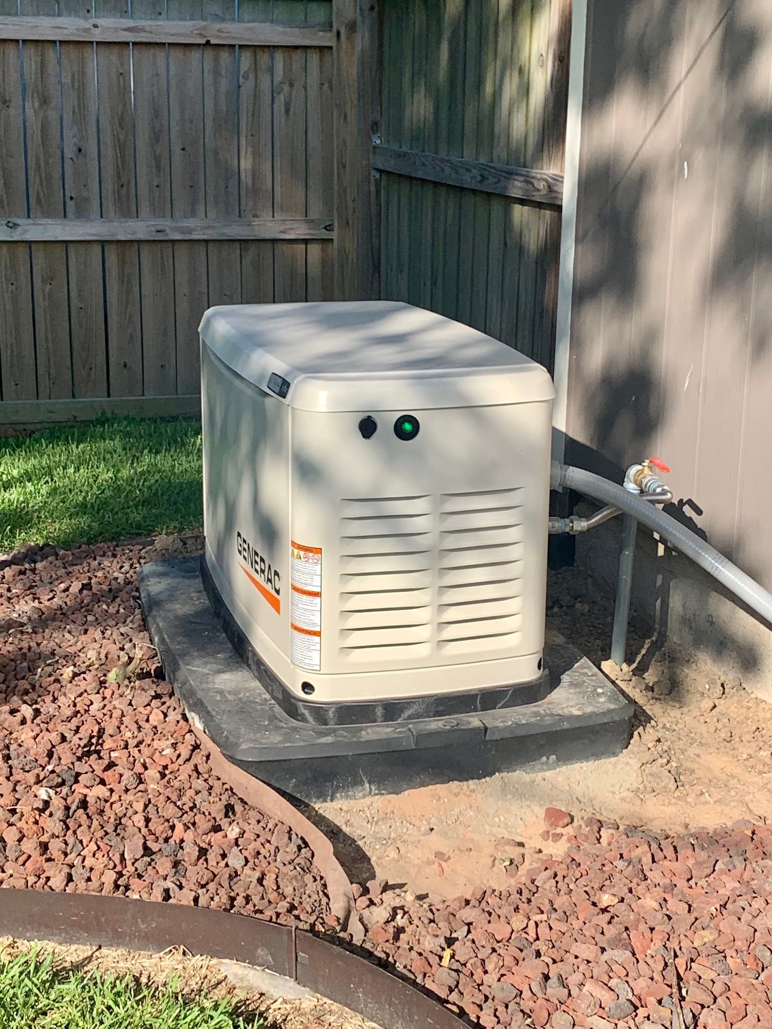 A generator is sitting outside of a house next to a fence.