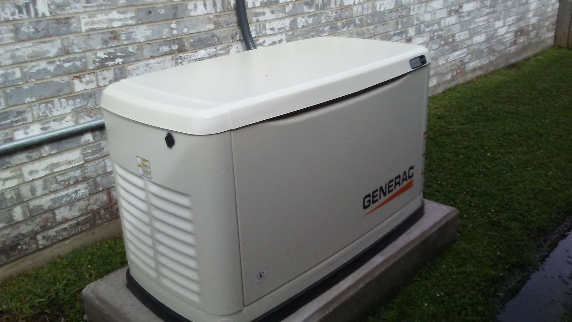 A generator is sitting in front of a brick wall.