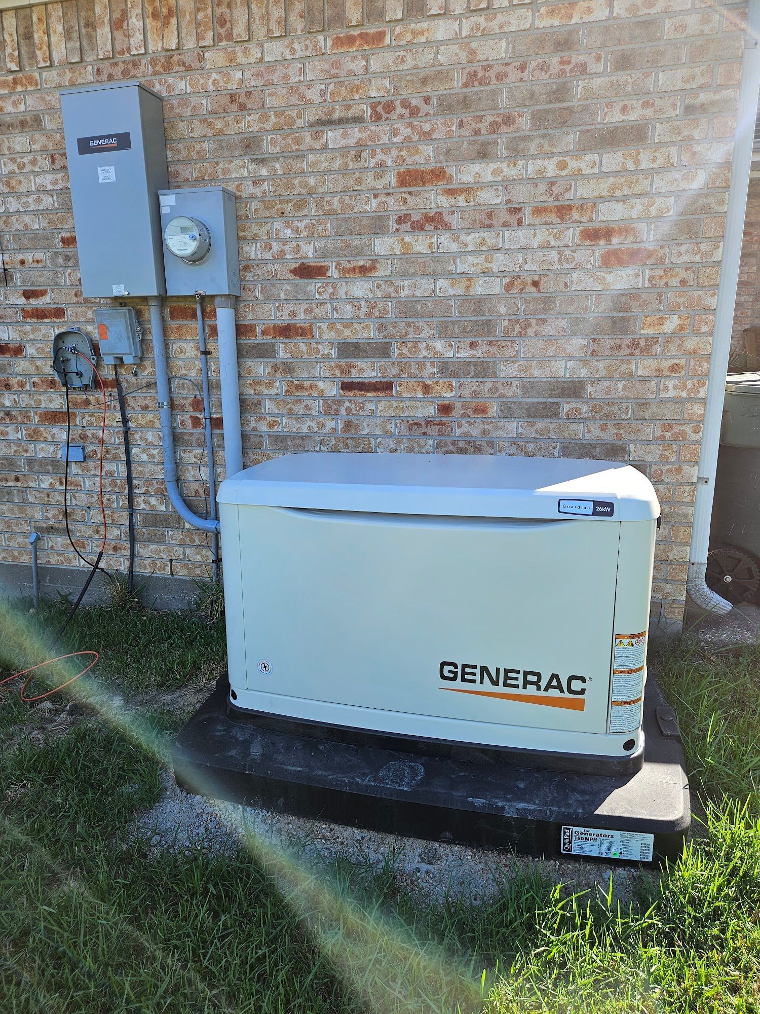 A generator is sitting on the side of a brick building.