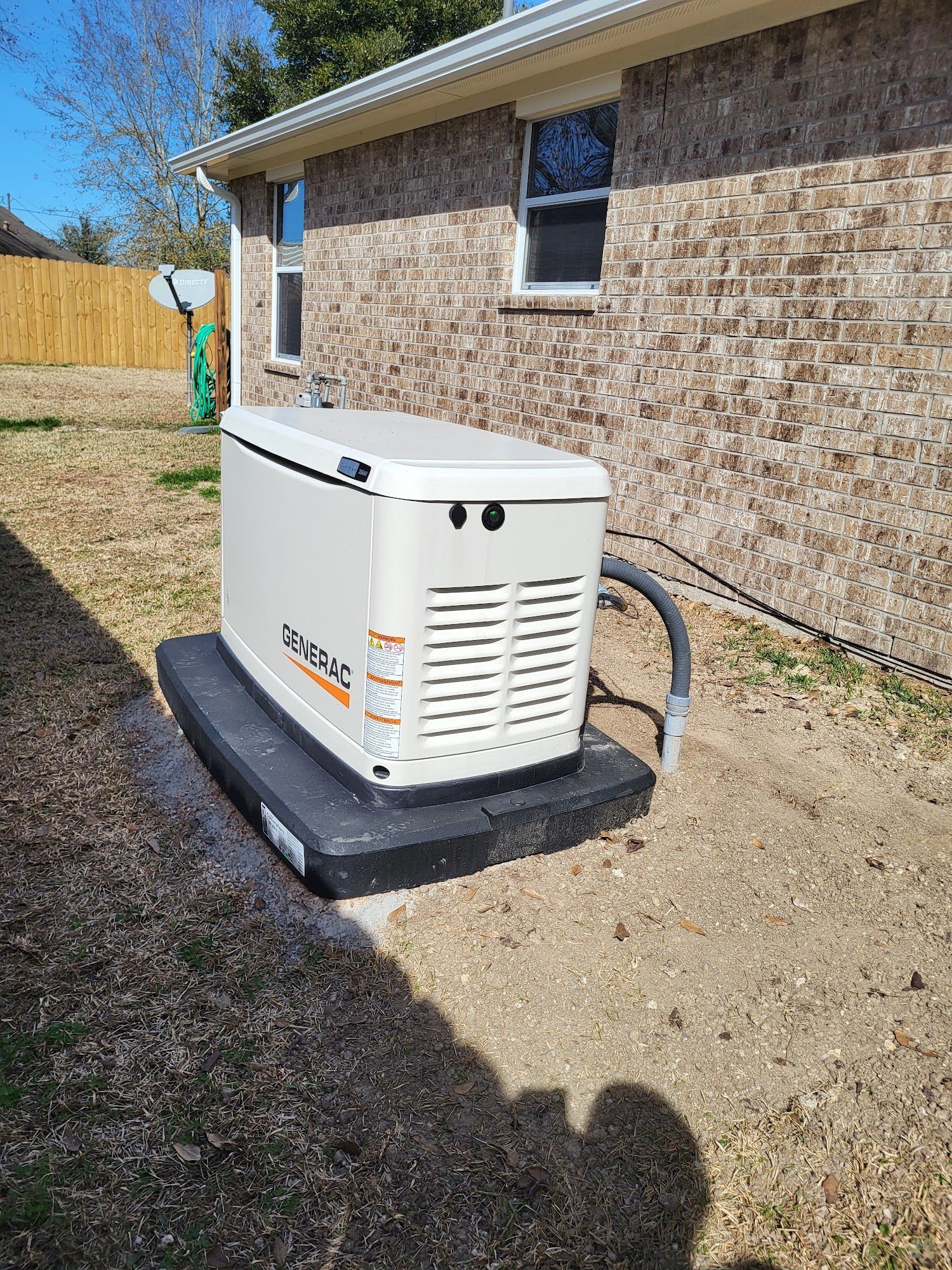 A generator is sitting in the backyard of a brick house.