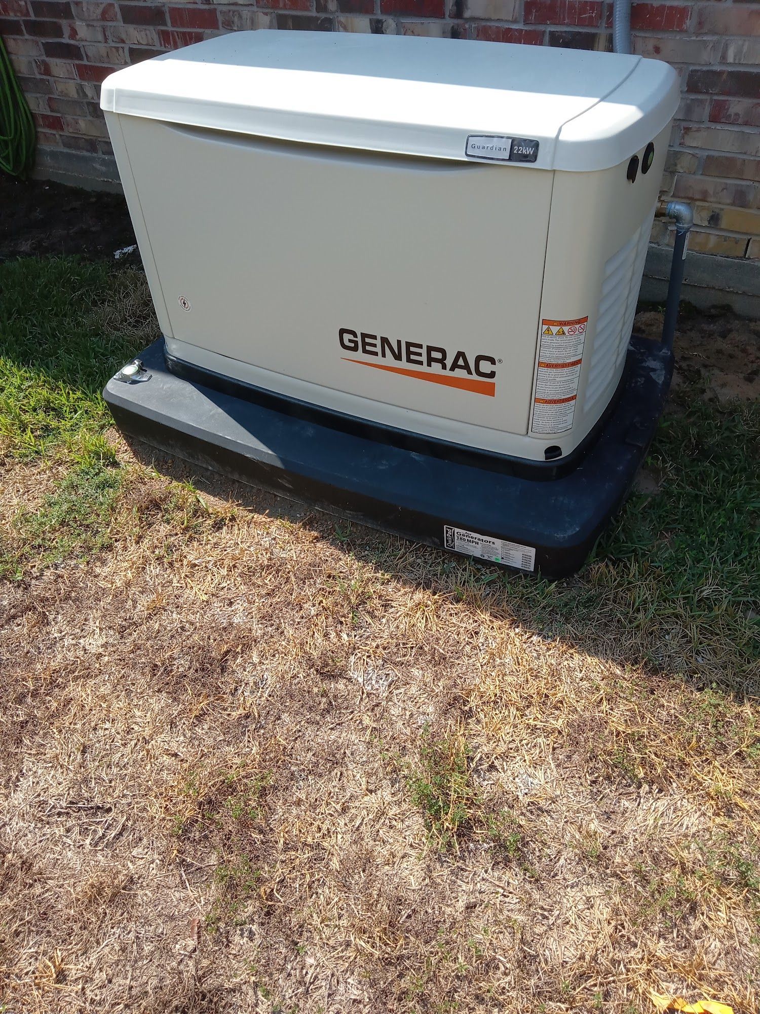 A generator is sitting in the grass in front of a brick building.