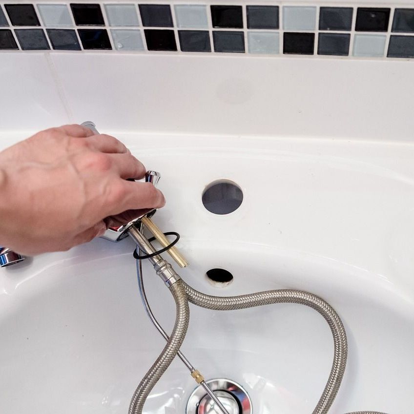 A person is fixing a faucet in a bathroom sink