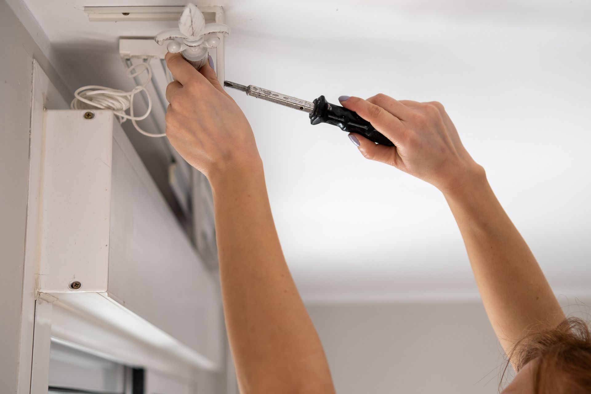 Persona che utilizza un cacciavite per lavorare su una tenda bianca fissata al soffitto.