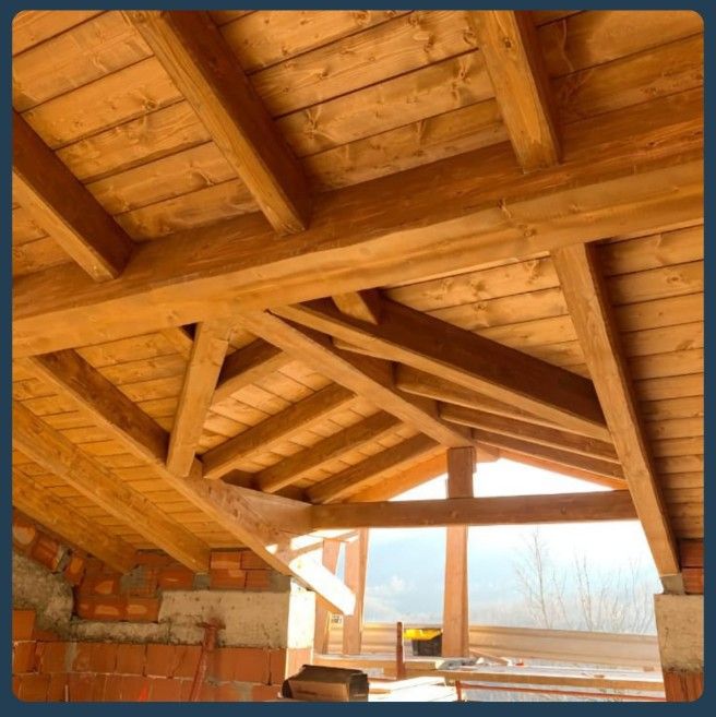 Struttura del tetto in legno, con travi e travicelli in tonalità calde, costruita su mattoni e cemento.