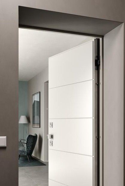 Porta interna bianca, parzialmente aperta. La porta presenta linee orizzontali. È visibile un corridoio con sedia e lampada.