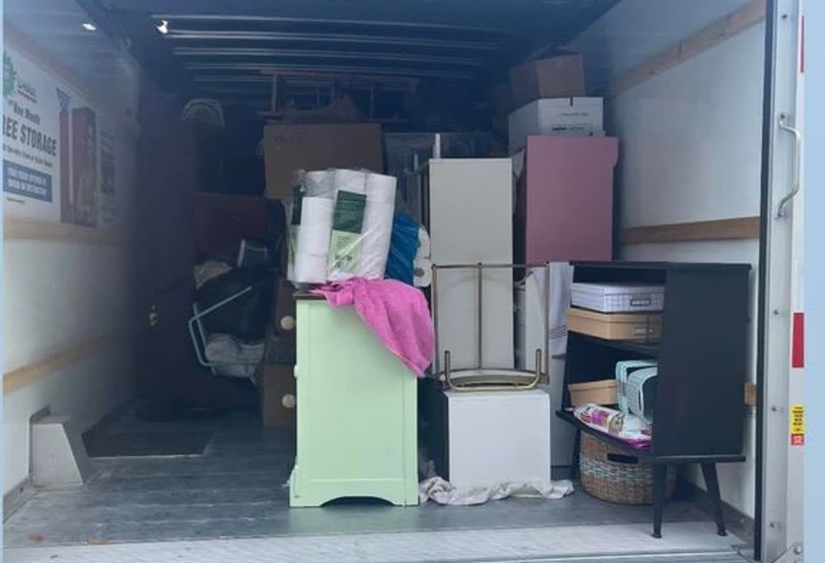 Packed storage unit with stacked boxes, furniture, and miscellaneous items inside an open trailer.