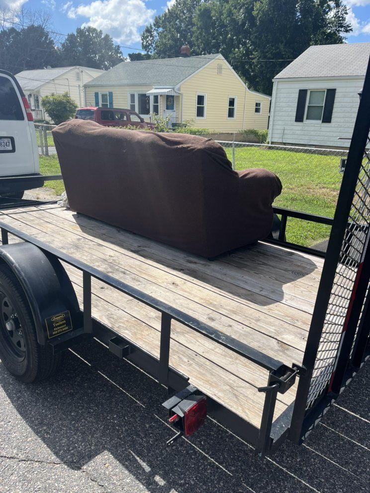 Brown couch on a utility trailer in a residential driveway, with houses in the background.