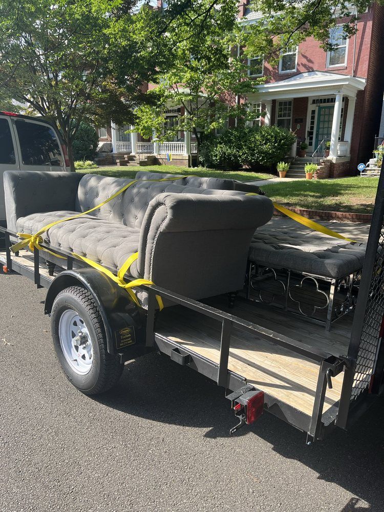 Gray couch strapped to a utility trailer parked on a residential street