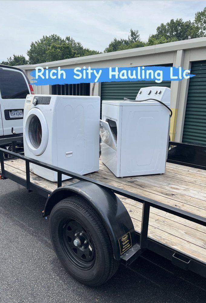 Two damaged white appliances on a flatbed trailer outside Rich Sity Hauling LLC