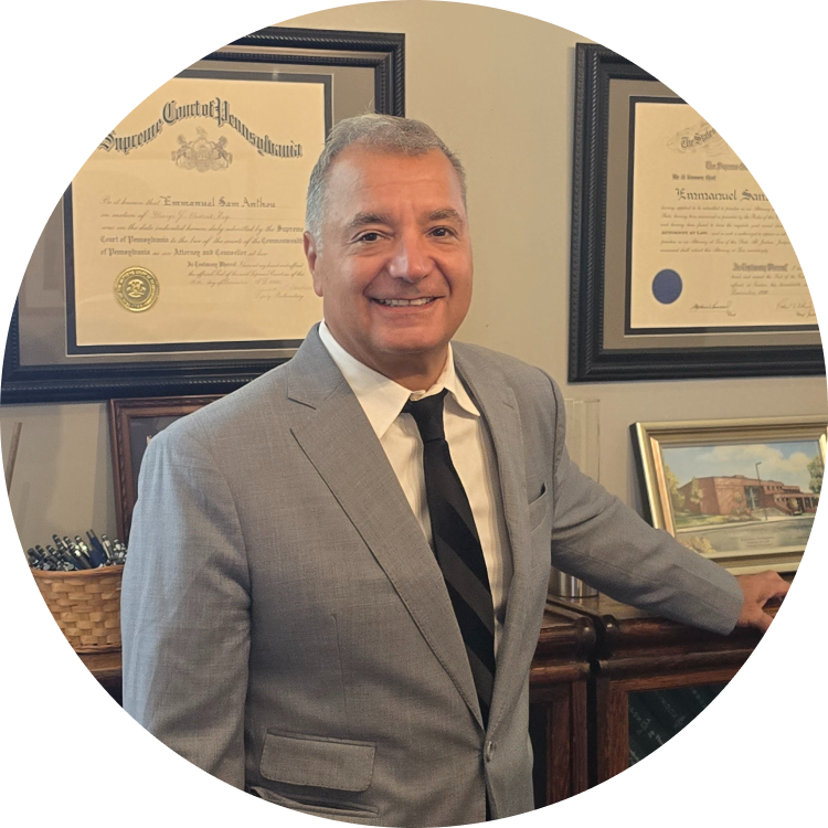 Man in a gray suit smiles, leaning on a wooden cabinet, diplomas behind him.
