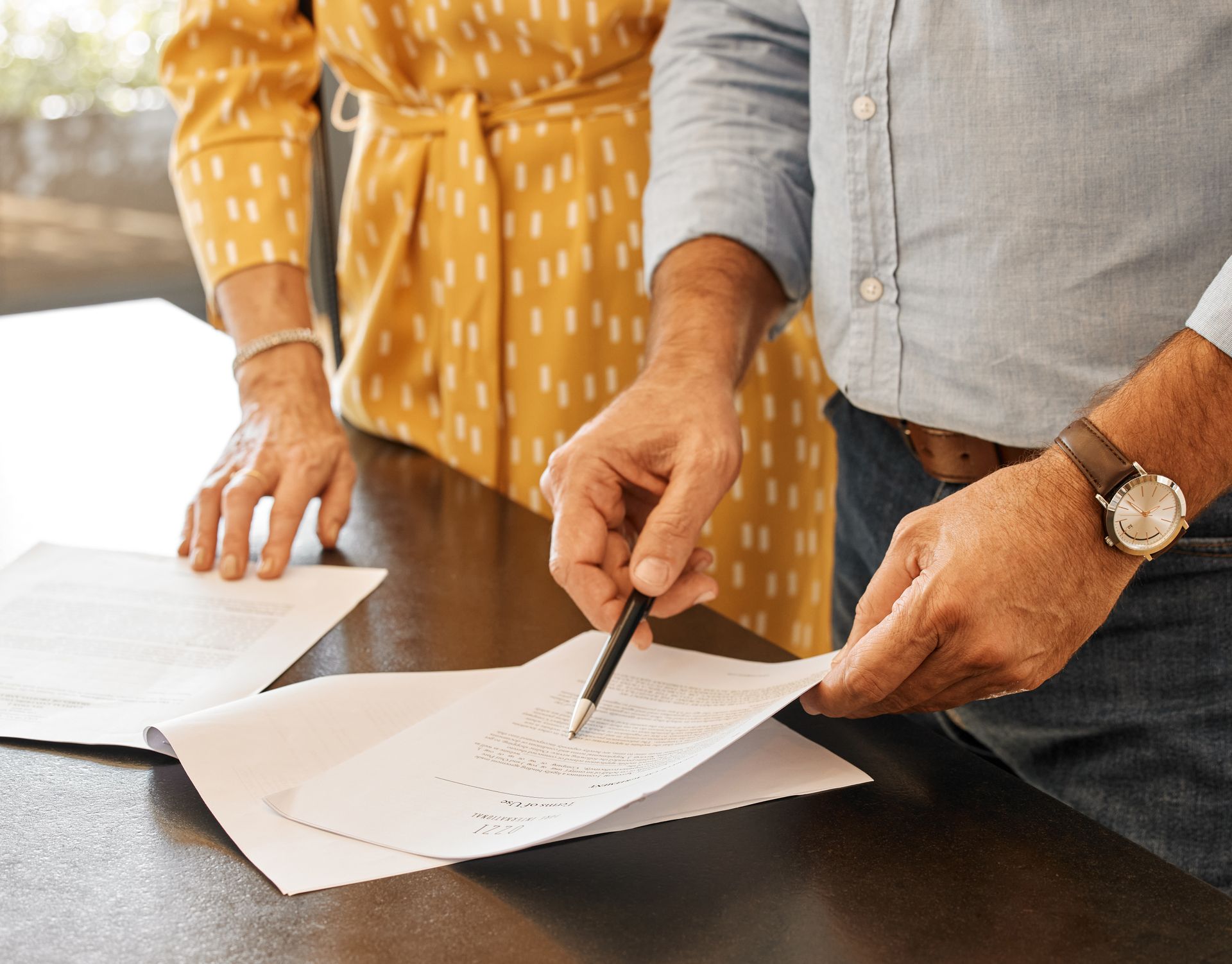 Man pointing at document, woman standing nearby; reading paperwork.