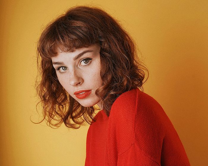 A woman with curly hair is wearing a red sweater and red lipstick.