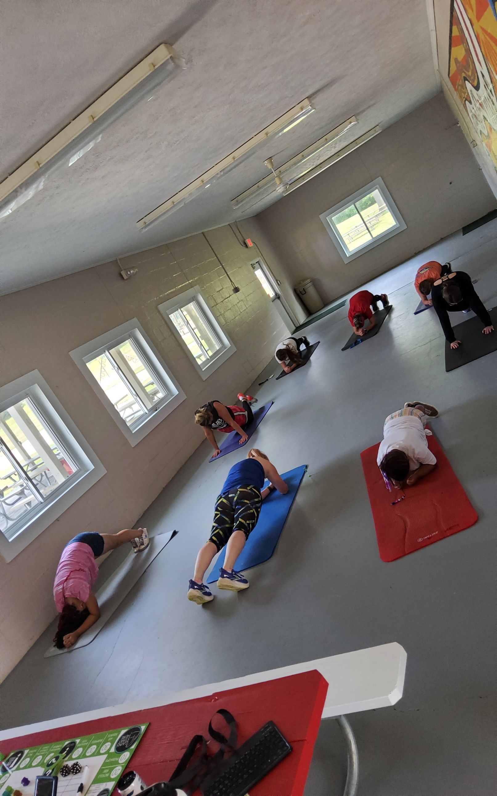 People doing yoga on mats in a bright room with windows and a colorful wall.