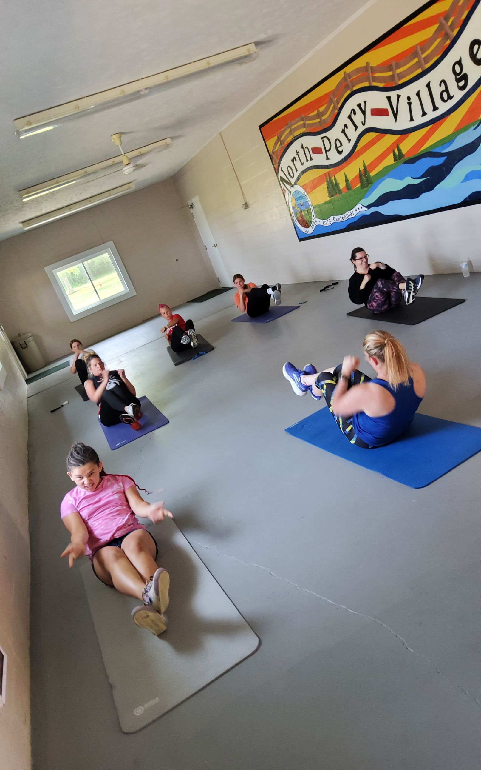People doing sit-ups on mats in a brightly lit room with a mural.