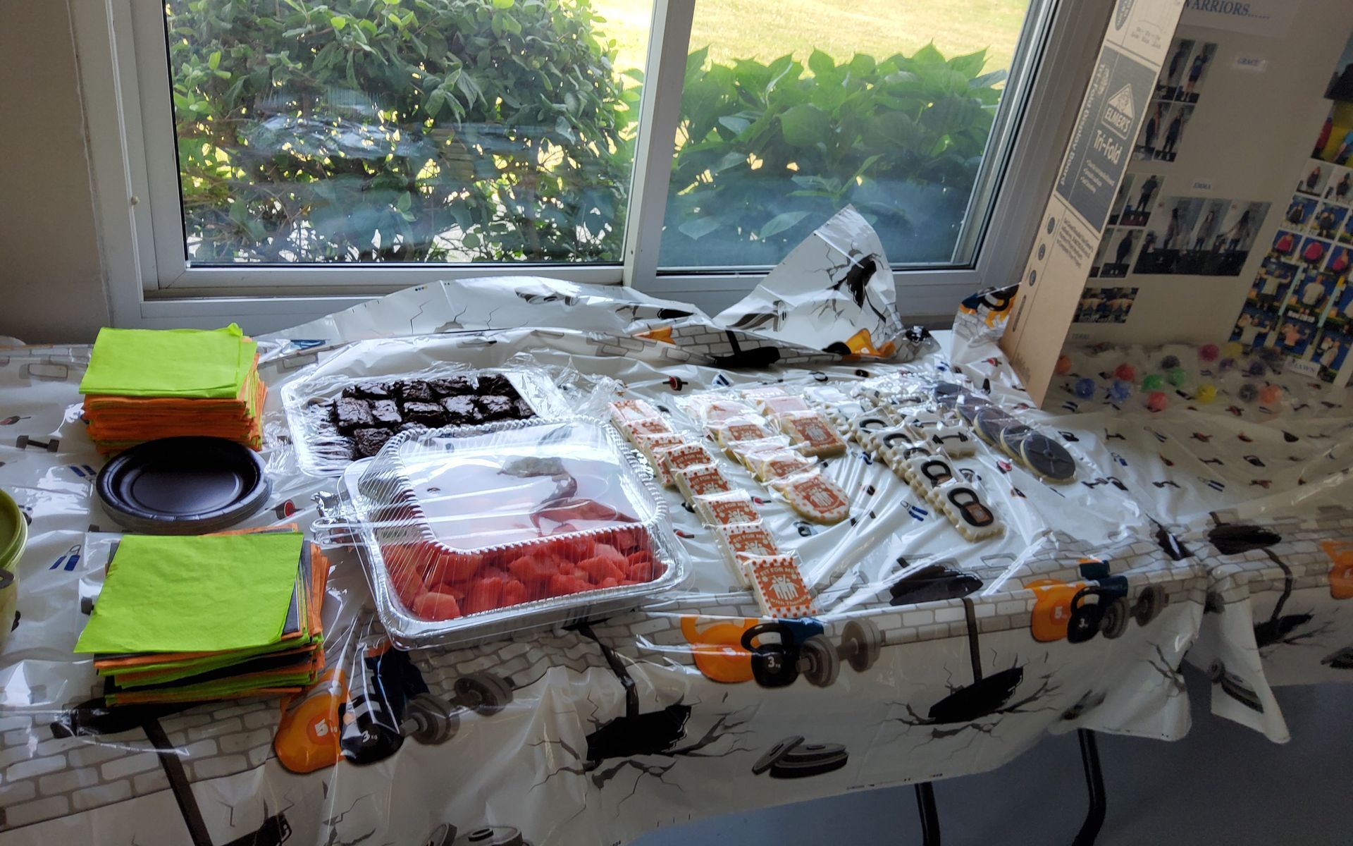 Sushi, snacks, and napkins on a table covered with a Halloween tablecloth next to a window.
