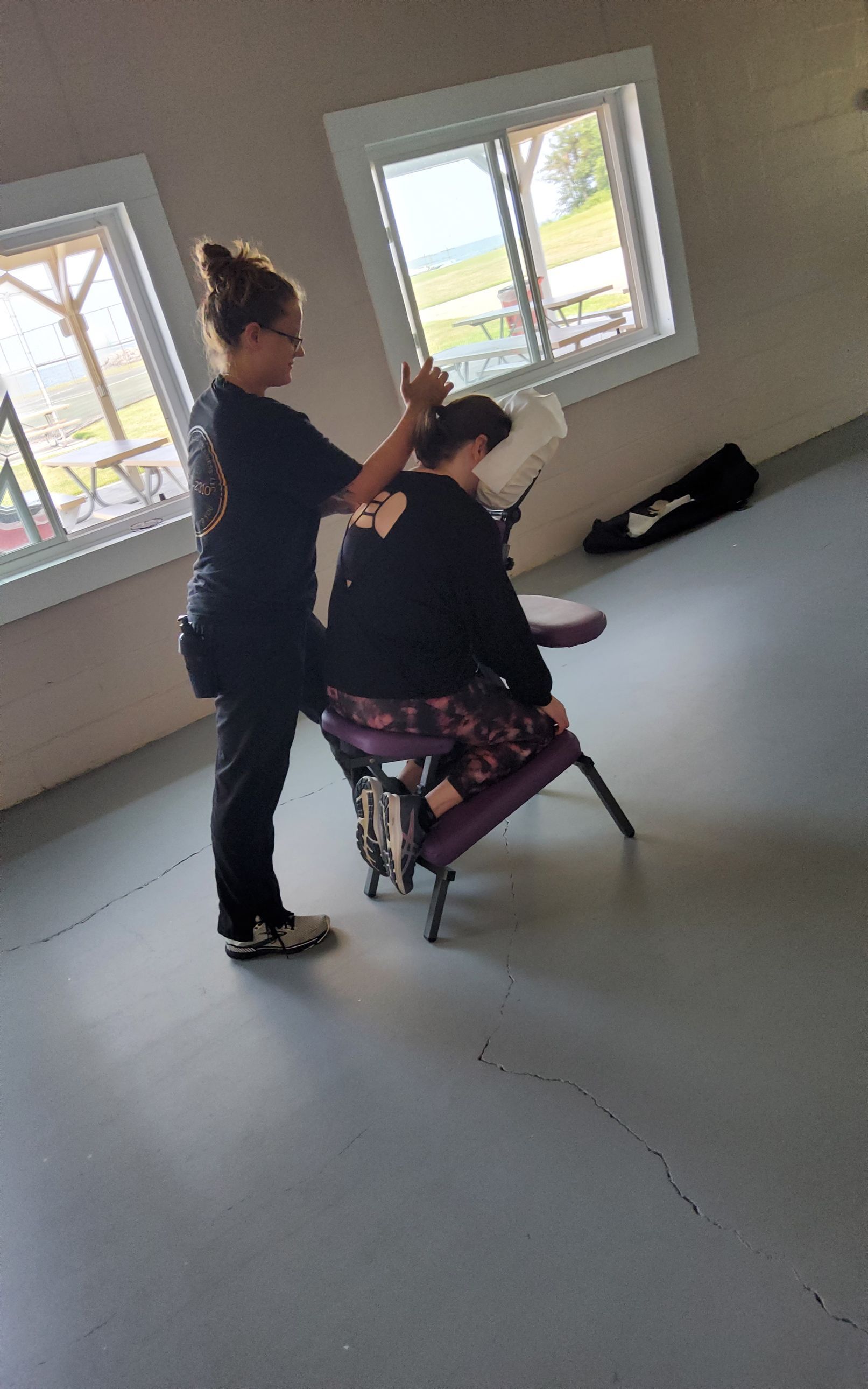 Person receiving a massage from another person in a massage chair. Interior setting, natural light.