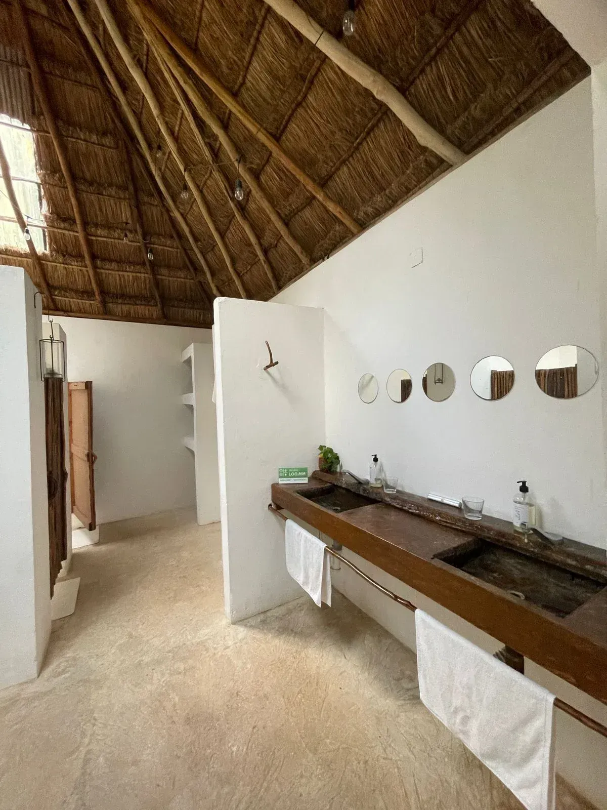 Bathroom with a thatched roof, wooden vanity, white walls, and round mirrors.