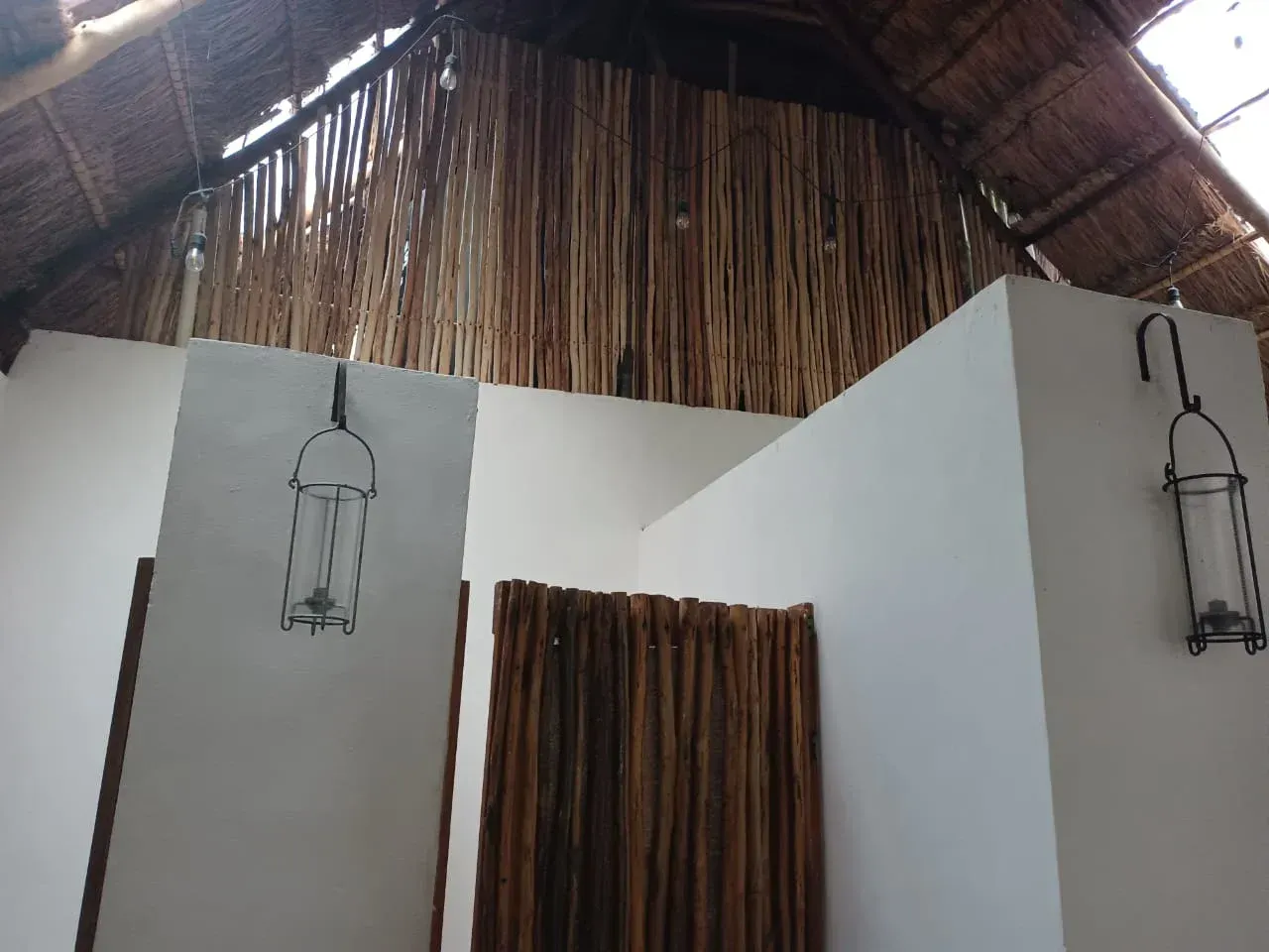 Paredes blancas con faroles colgantes y detalles de madera, ducha al aire libre con techo de paja.