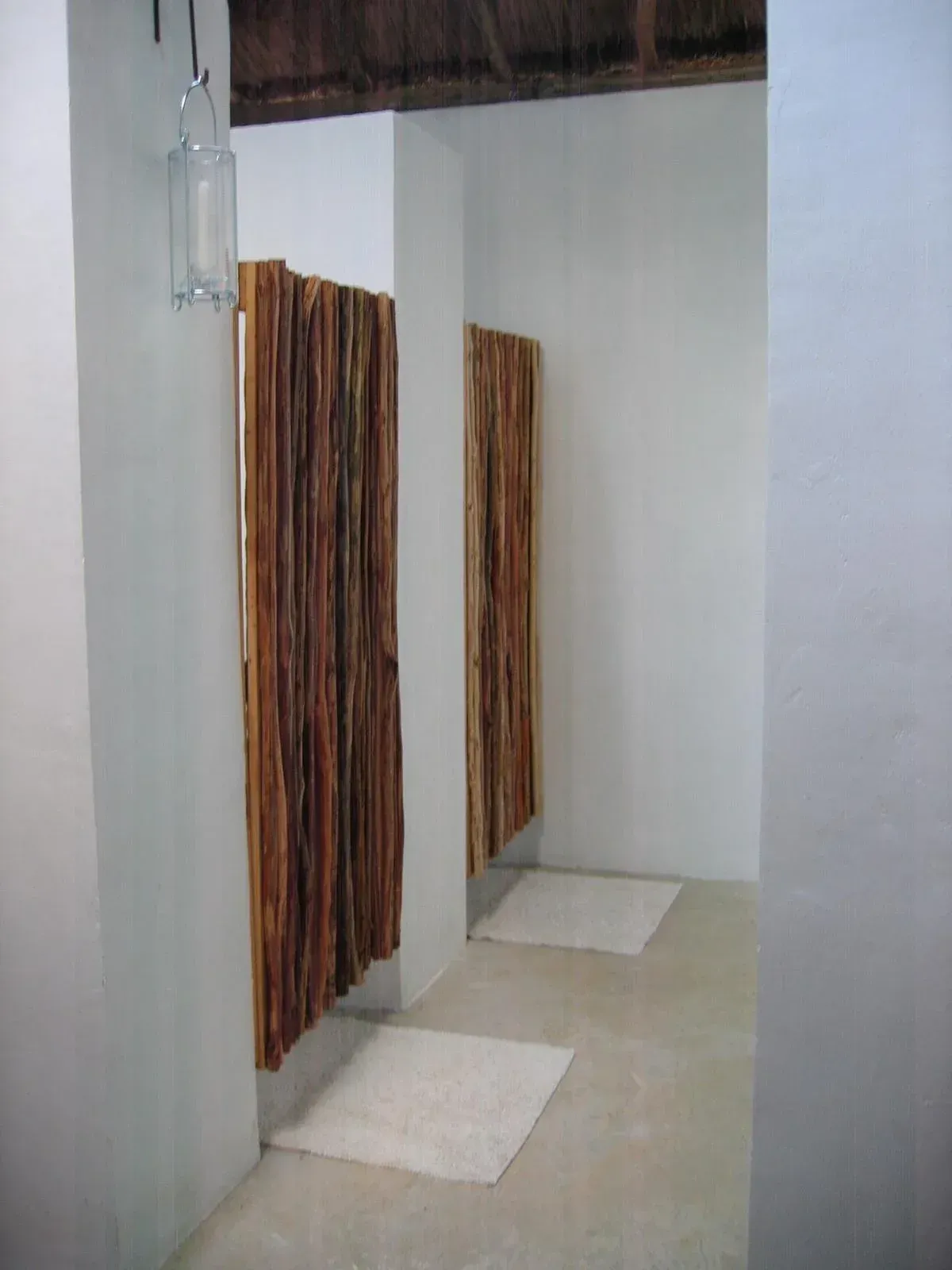 Two shower stalls with wooden walls, white walls, and rugs on a concrete floor.
