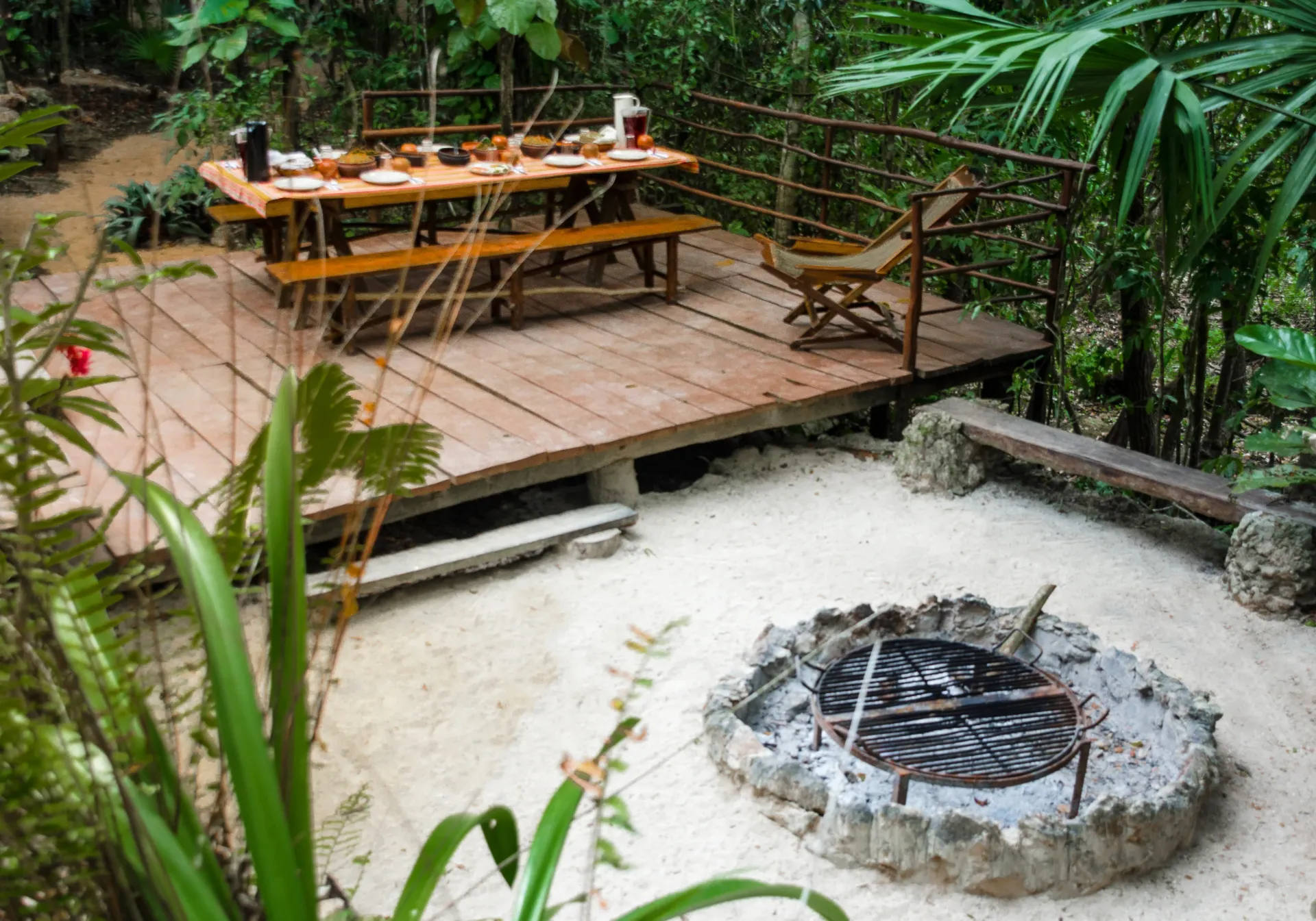 Área de comedor  de madera al aire libre:  con  mesa lista  para comer, fogata, rodeado de exuberante vegetación.