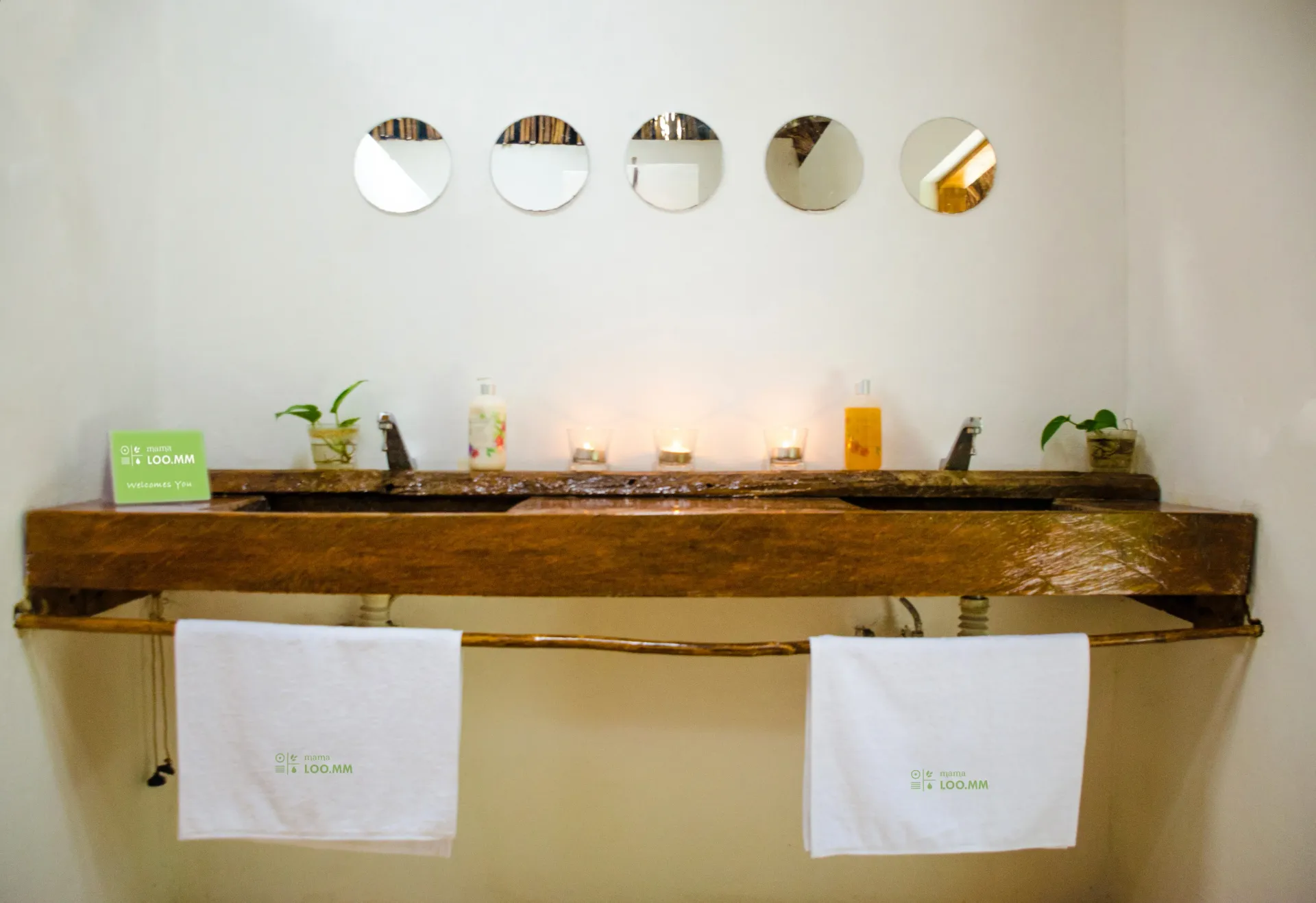 Baño rústico con lavabo doble de madera, espejos circulares y toallas.