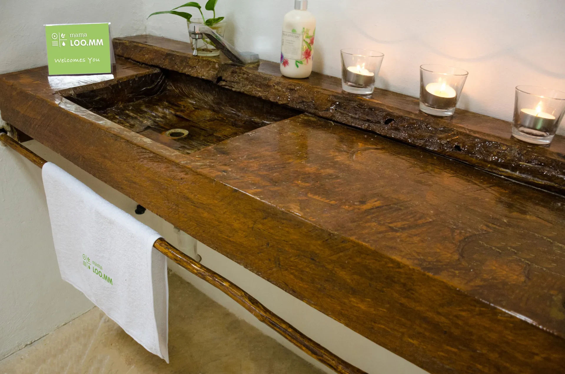 Tocador de baño rústico de madera con lavabo, estante, velas y toalla.