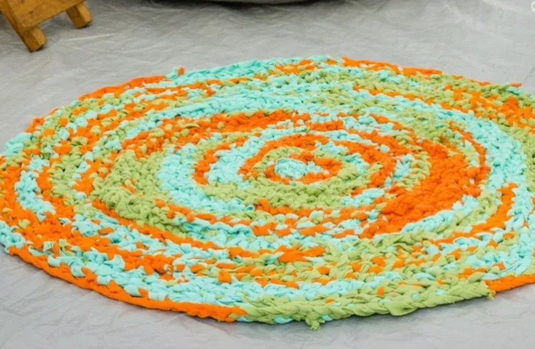 Alfombra de forma ovalada en tonos naranja, azul y verde, con dibujo en espiral.