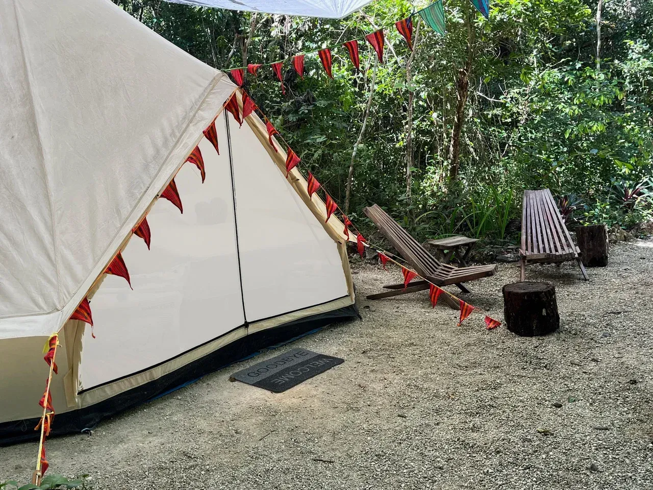 White tent with red flags, camping setting with a chair and trees.