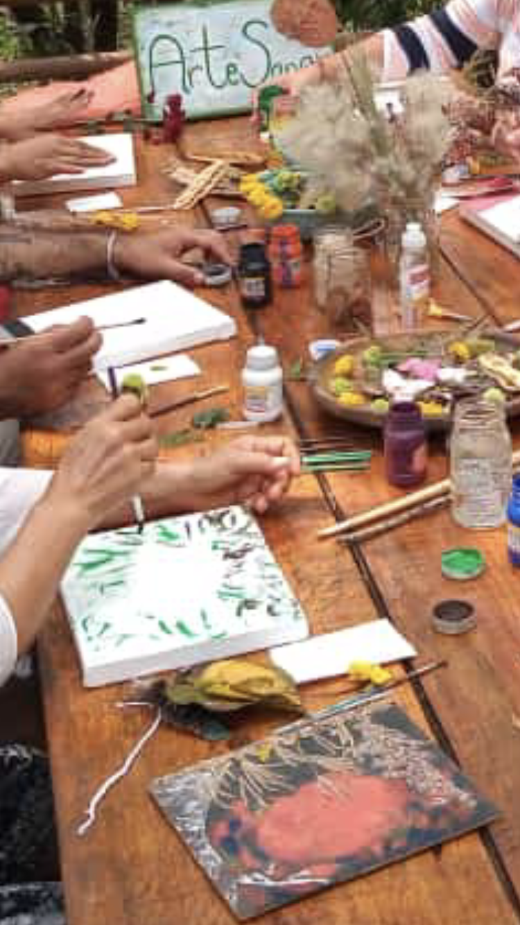 Personas pintando sobre lienzo al aire libre en una mesa con materiales de arte.