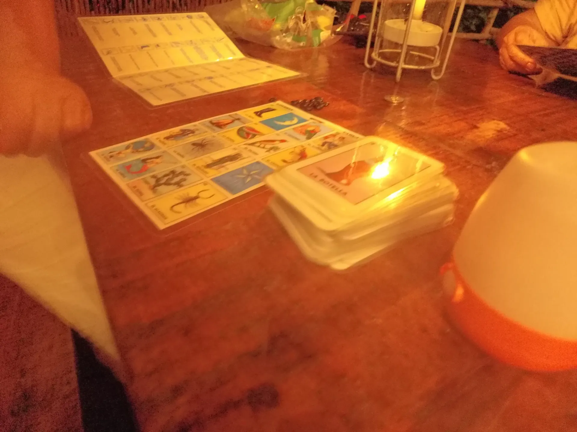 Mesa de madera con tablero de juego, cartas y una pequeña lámpara.