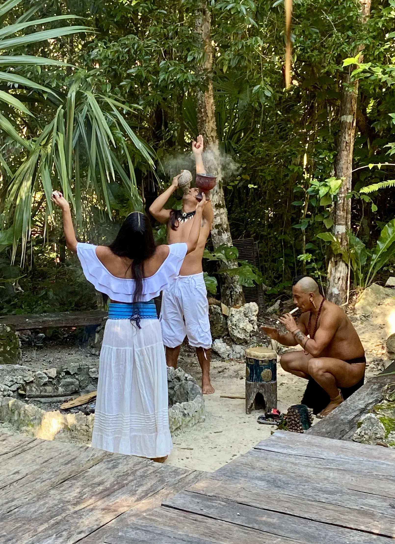Personas realizando un ritual en la selva. Una mujer vestida de blanco con los brazos en alto, hombres con humo.