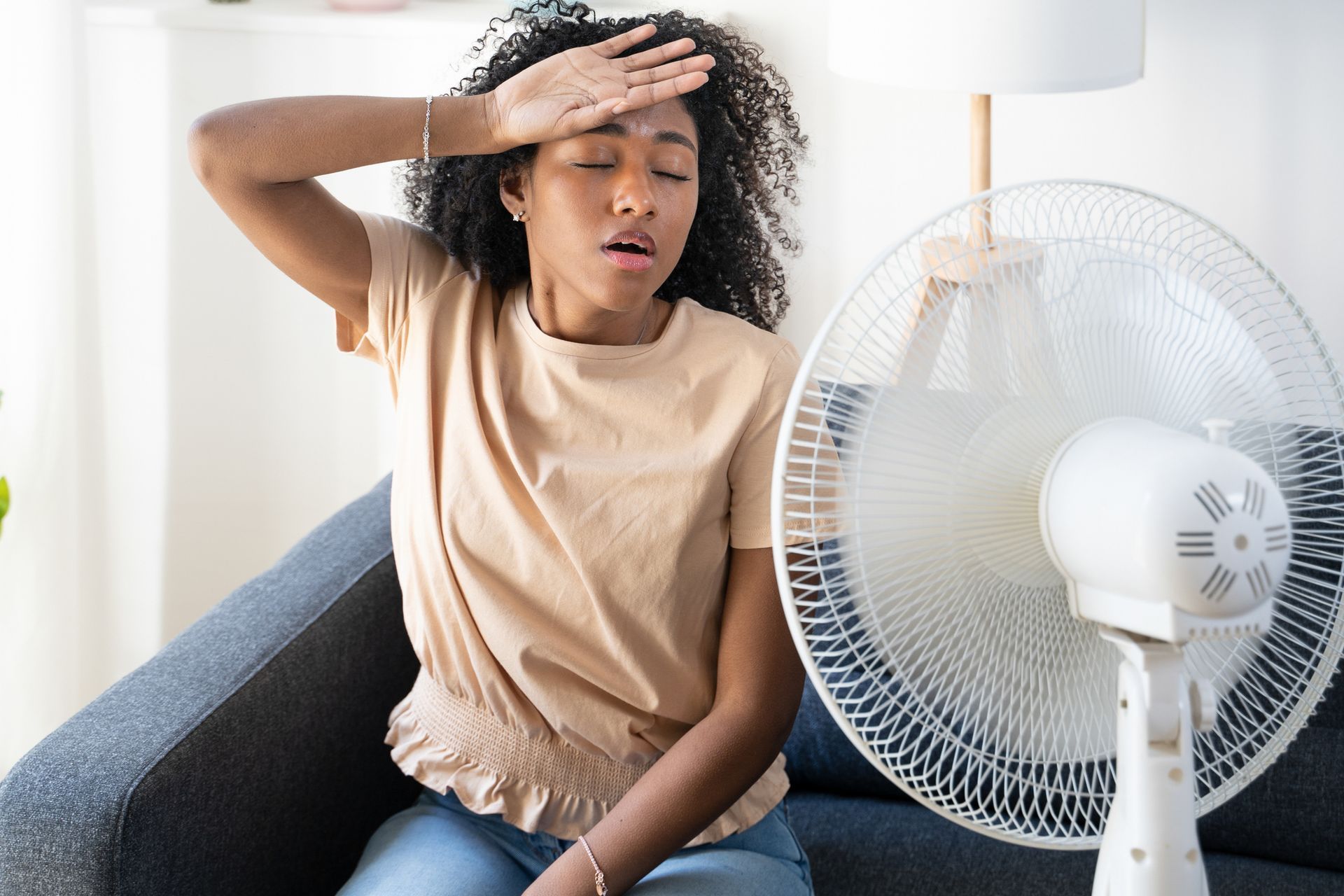 Woman cooling off indoors during hot Florida summer due to failing air conditioner.