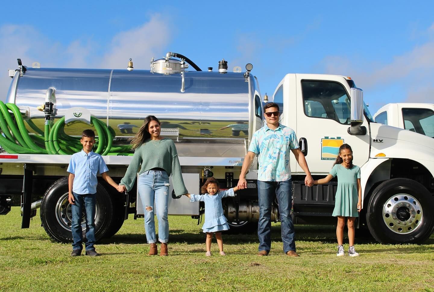 Family standing beside a shiny silver truck on grass under a clear blue sky