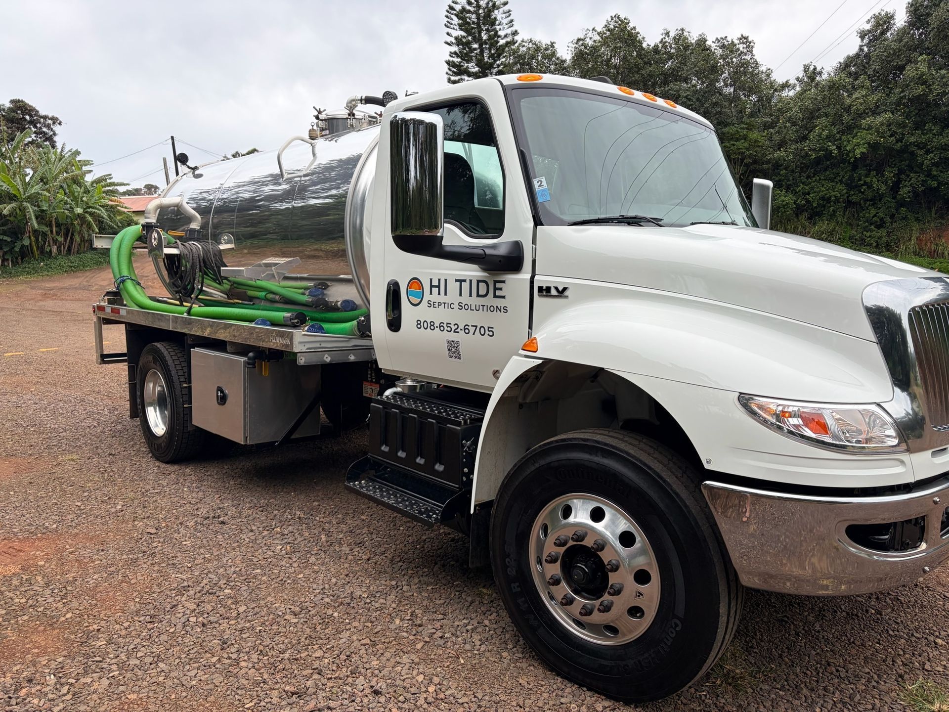White H2 Tide vacuum truck parked on a gravel lot with greenery in the background