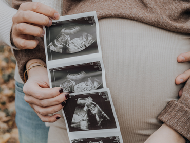 Hands holding ultrasound prints against a pregnant belly in a beige sweater