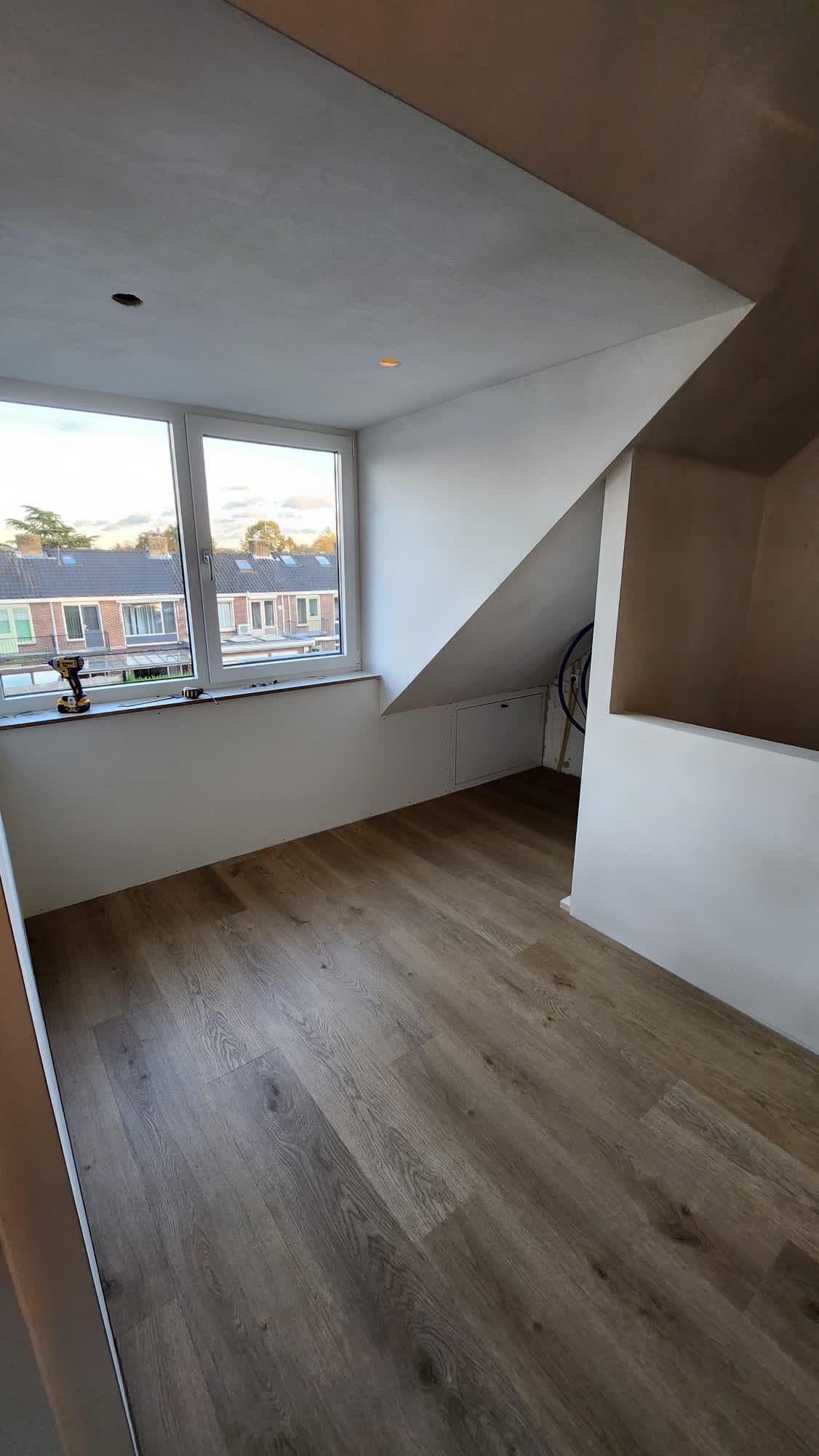 een lege kamer met een raam en een houten vloer