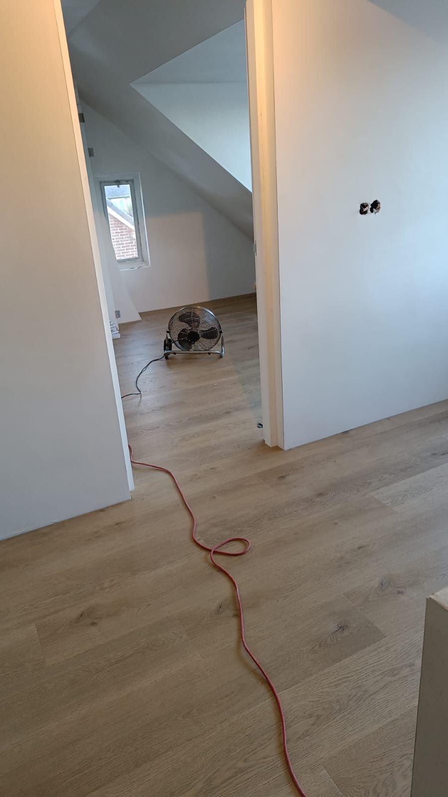 een ventilator zit op een houten vloer naast een rood snoer