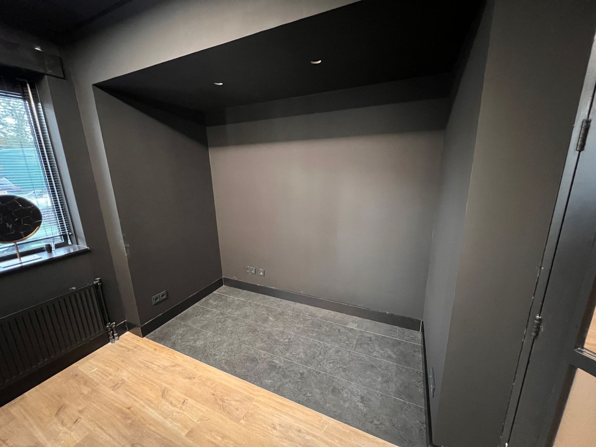 een lege kamer met zwarte muren en een houten vloer