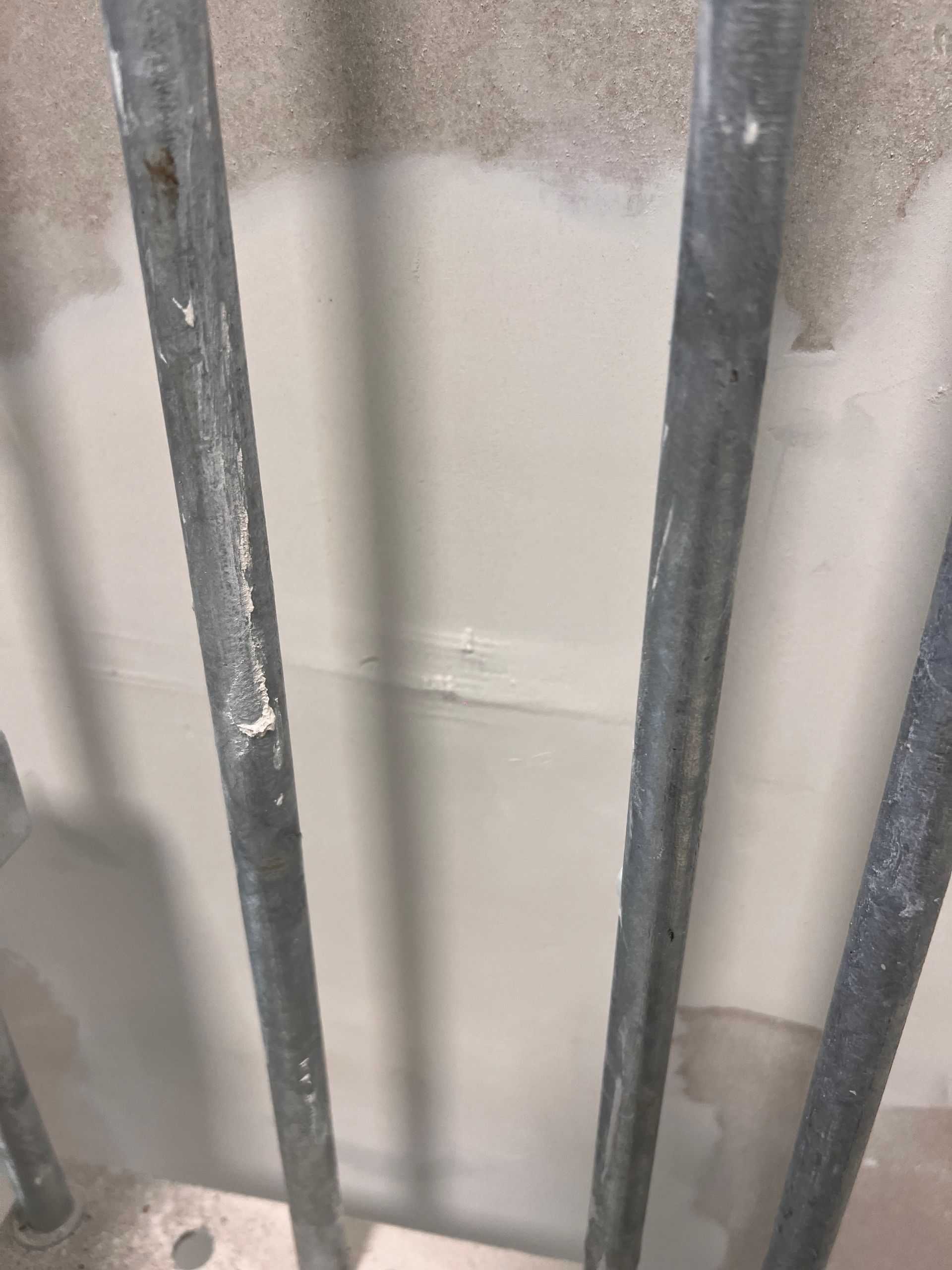 een metalen reling met daarachter een witte muur