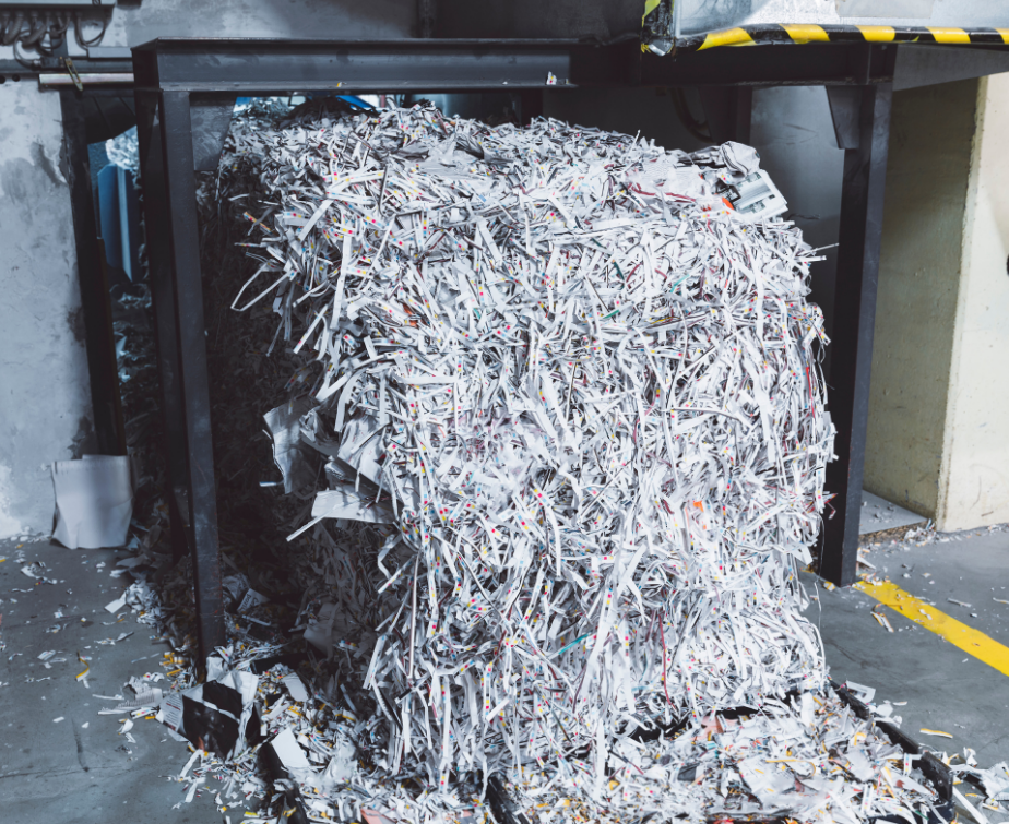 A large, densely packed bale of shredded white paper sits inside a metal frame on a factory floor.