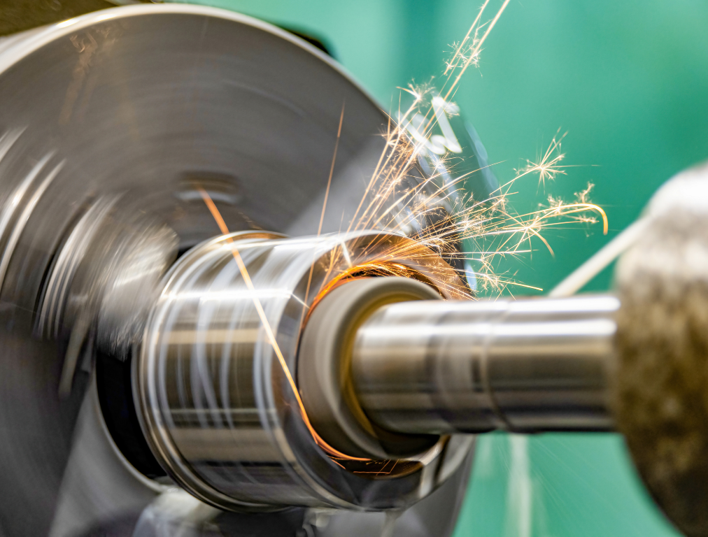 A close-up of a metal part being machined on a lathe, with bright orange sparks flying during the cutting process.