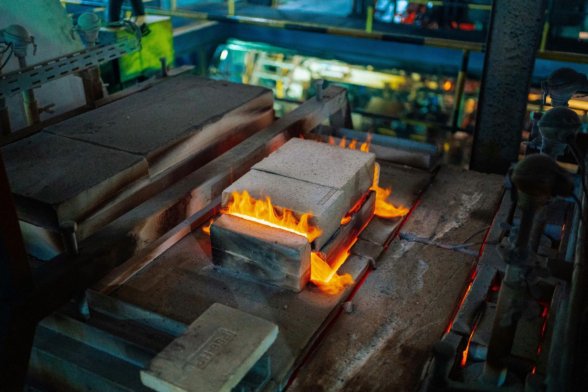 Glowing orange flames lick the sides of stacked refractory bricks in a dark industrial furnace setting.