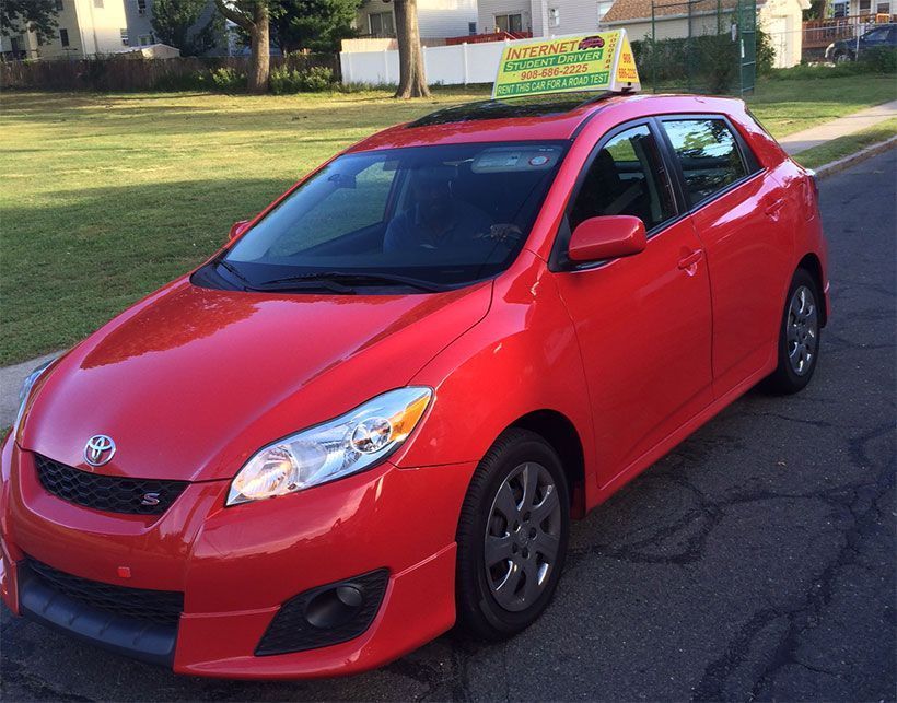 Red Toyota Matrix with driving school sign on the roof, parked on a street.
