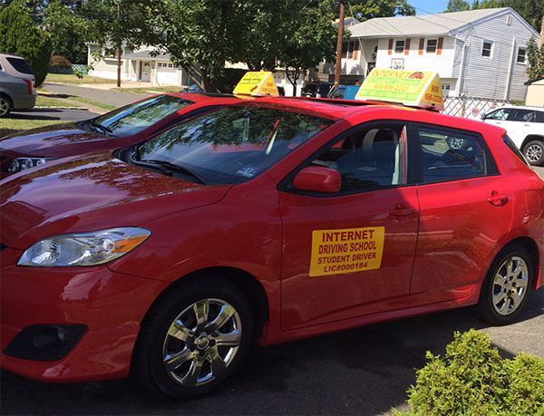 Red driving school car parked on a residential street with a sign on the roof.