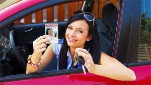 Woman in red car holding driver's license and keys, smiling.