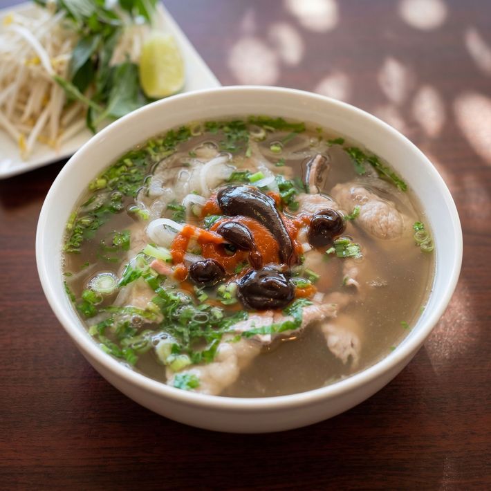 Bowl of steaming noodle soup topped with herbs and mushrooms on a wooden table